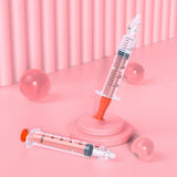Two syringes with orange caps on a pink background