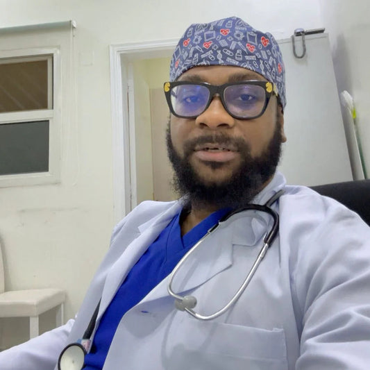 Doctor wearing a white coat, blue scrubs, and a patterned cap with a stethoscope around his neck.